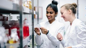 Two science students in lab coats happily look at the results on a petrie dish 