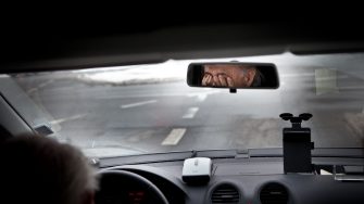Tired driver rubbing eyes in car's rear-view mirror