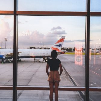 Young woman standing in airport, looking out of window at plane