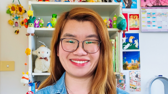 Amy stands smiling in front of a cabinet filled with colour curios