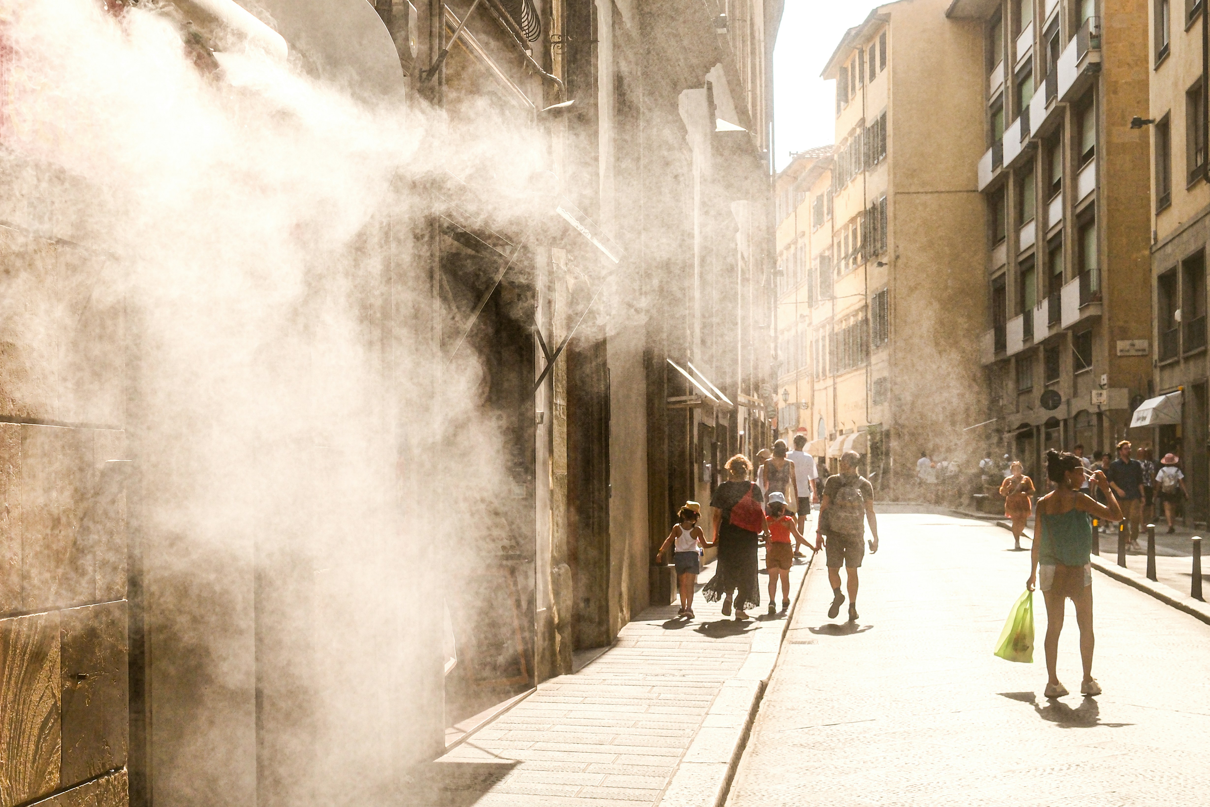  Summer street scene in Firenze, Italy, during a heatwave. People walking under the strong Tuscan sunlight with refreshing water mist in the urban atmosphere.