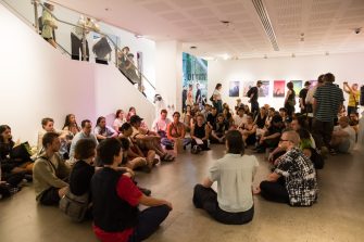 A group of people sitting in a circle in a gallery space for the A&D Annual 2023 exhibition. 