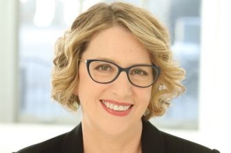 Amanda Anderson, a middle-aged white woman with short blonde hair and spectacles. She smiles brightly.