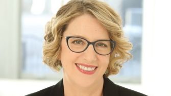 Amanda Anderson, a middle-aged white woman with short blonde hair and spectacles. She smiles brightly.
