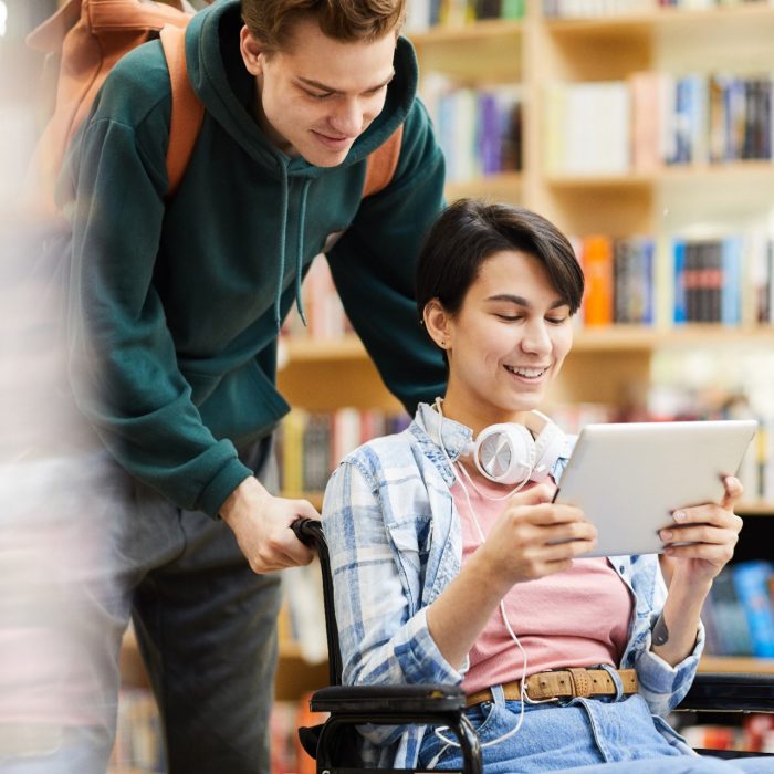 Man in library pushing wheelchair with student learning on tablet 