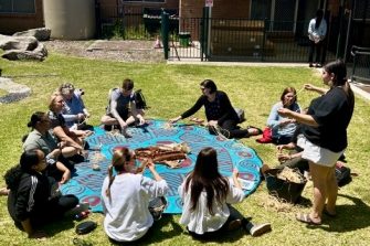 Group of people sitting in a Yarning circle outside at Matraville Sports High School