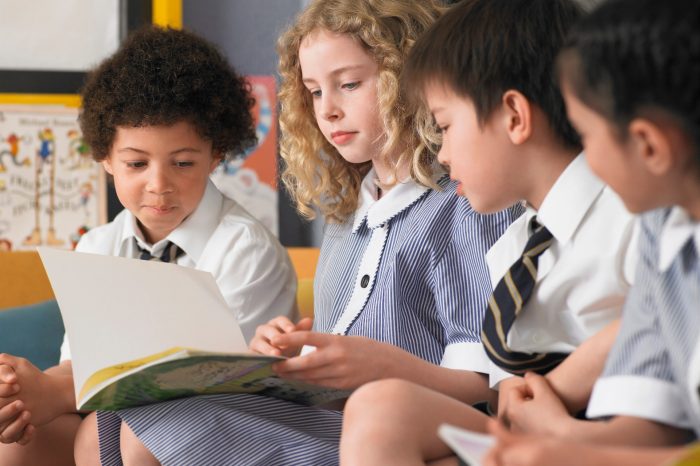 Row of Primary students reading book sitting in classroom