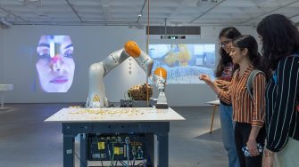 Three students interact with a robot arm, sweeping small object.s