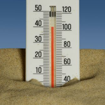 A plastic thermometre wedged in sand shows a high temperature