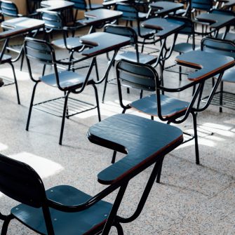 A wide angle shot captures an empty school classroom, featuring rows of uniform, blue tables and chairs on grey flooring.