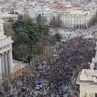 A wide arial camera shot captures a mass protest storming the streets of Madrid.