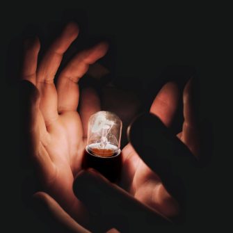 A close crop image captures a pair of hands cradling a lightbulb in a darkened space.