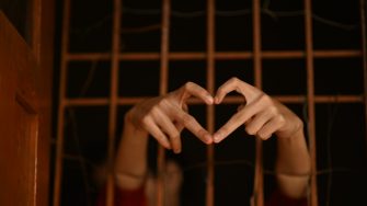 A person reaching through bars with a hand gesture of a love heart