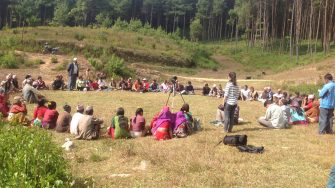 Research group in Nepal sitting in a circle on grass with forest plantation in the background