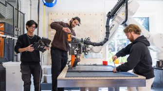 Three students working with a robotic arm in a lab, adjusting components and programming the machine