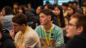 A group of university students wearing yellow lanyards listening attentively during a lecture or seminar