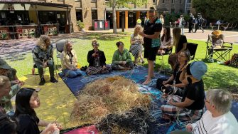 A group of people sitting in a circle outdoors, weaving natural fibres as part of an Indigenous knowledge-sharing workshop.