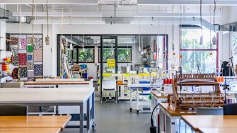 A bright fashion design studio with large tables, sewing machines, colorful fabrics, and tools for students to work on projects.