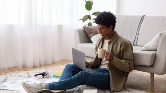 Teenager using laptop and drinking coffee during his online studies at home