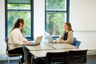 Two students with laptops sitting across from each other