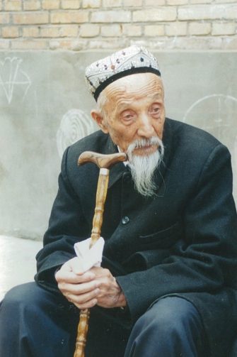 Uyghur elder with flower cap and walking stick
