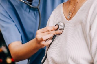 Lady coming to clinic for heart and lungs checkup, male doctor using stethoscope, listening to female patient's breath or heartbeat, sitting in clinic office