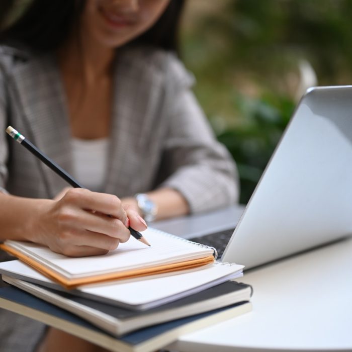 Cropped shot of businesswoman working on laptop computer and making notes in a notebook.  