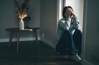 Depressed woman sitting on floor covering face with hands in despair