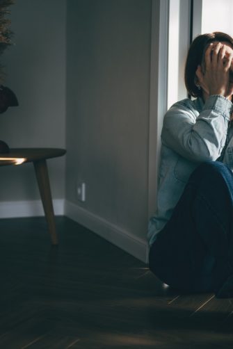 Depressed woman sitting on floor covering face with hands in despair