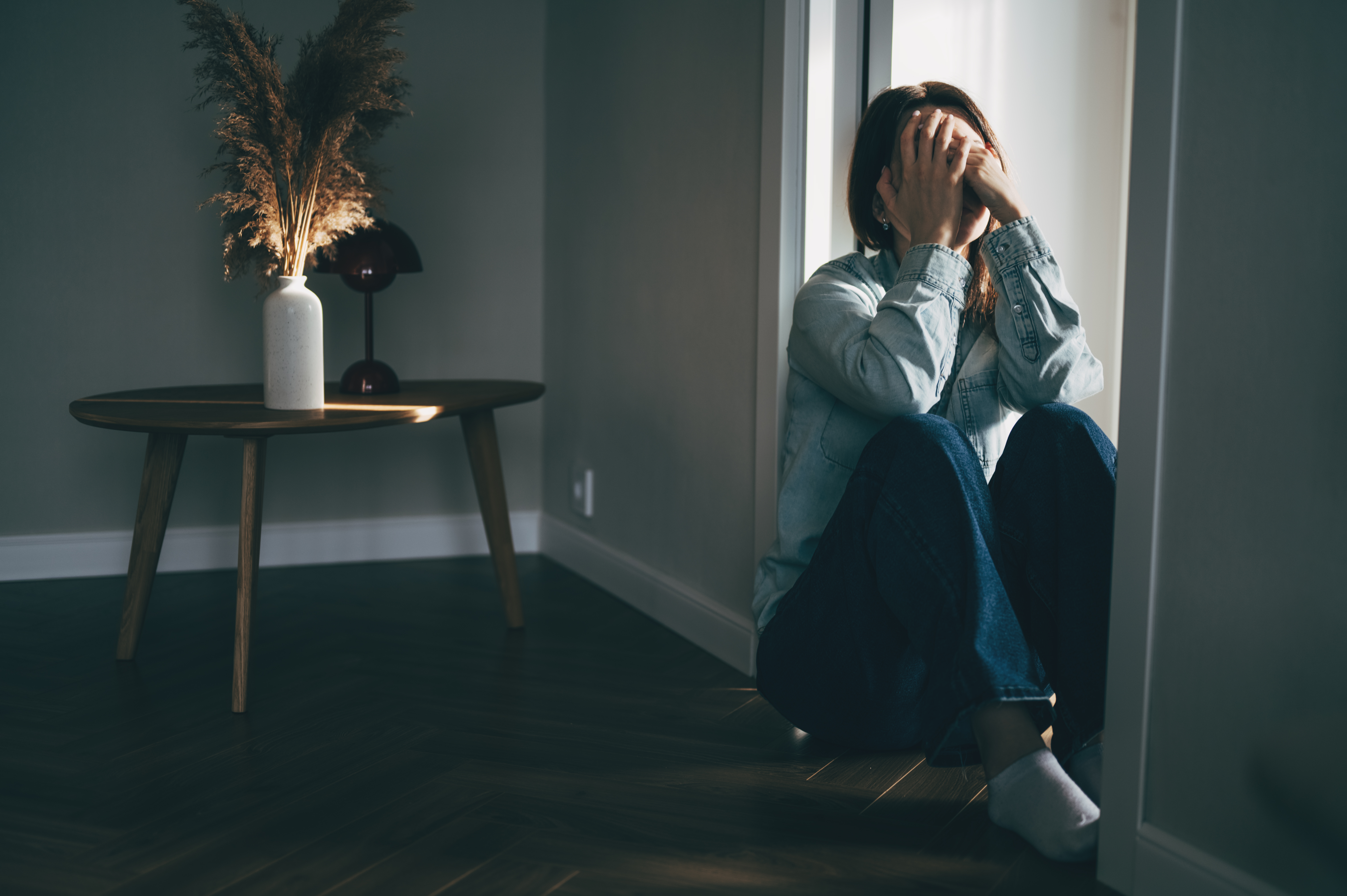 Depressed woman sitting on floor covering face with hands in despair