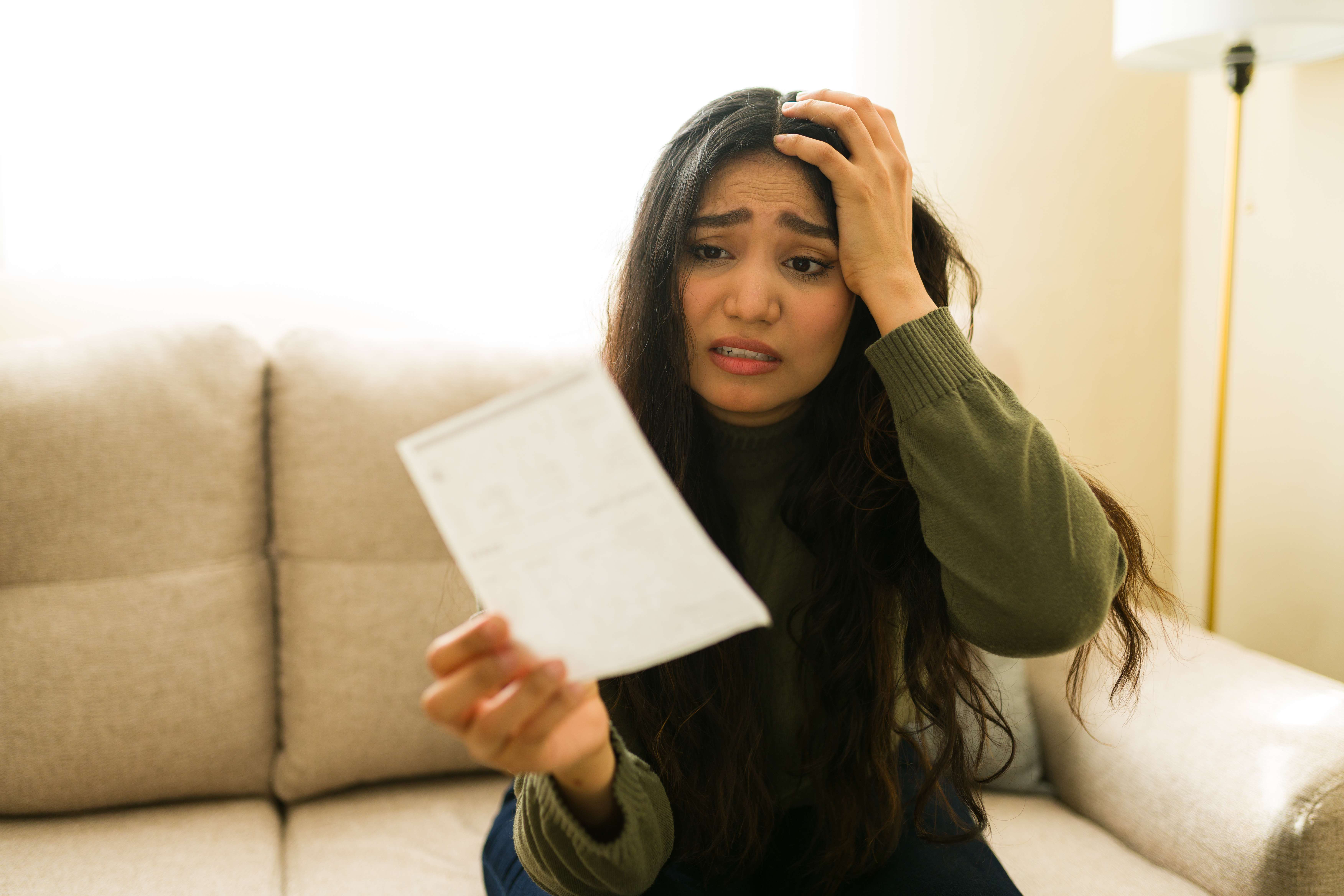 A woman looks distressed while holding a bill at home