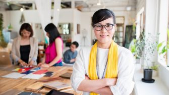 Portrait of a mid adult, female interior designer or architect looking into the camera whilst her team work away in the background.