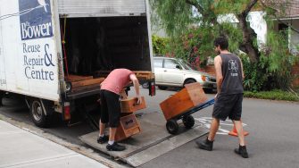 Two workers load wooden furniture onto a Bower Reuse & Repair Centre truck for reuse