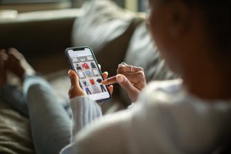 Person relaxing on a couch while browsing online shopping websites on a mobile device.