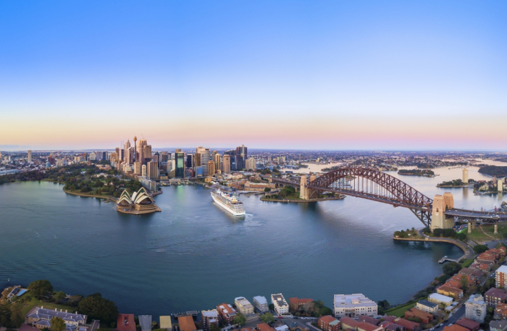 An aerial view of Sydney Harbour featuring the Harbour Bridge, the Opera House, and the city skyline.