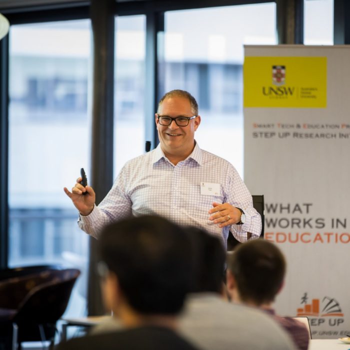 A speaker presenting beside the STEP UP Research Initiative banner at the UNSW Business School STEP UP 2019 conference.
