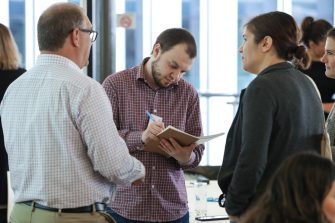 An attendee taking notes while talking with colleagues at the STEP UP 2019 conference.