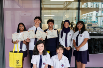 Students in white and navy uniforms holding UNSW Step Up certificates with a UNSW staff member and a UNSW Sydney tote bag at Arthur Phillip High School in 2022