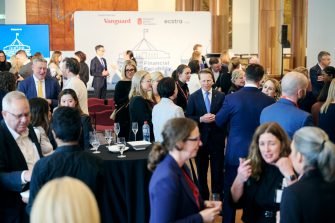 Guests network with drinks at the Power of Financial Capability event at Parliament House, in front of a backdrop supported by Vanguard, Financial Basics Foundation and Ecstra.