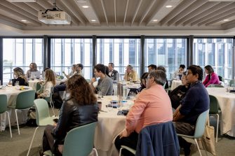 Delegates seated at round tables during the STEP UP 2026 conference in a light-filled UNSW room with floor-to-ceiling windows overlooking the city.