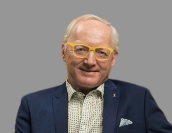 Professor Toby Walsh wearing yellow spectacles and a navy suit with a pocket square.