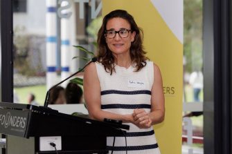Woman in white dress with black stripes standing at a lectern.