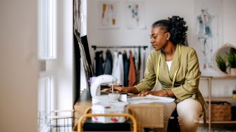 Young beautiful female clothing designer drawing sketches at workshop