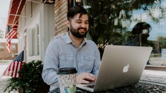 Man in gray denim dress shirt smiling while using Macbook 