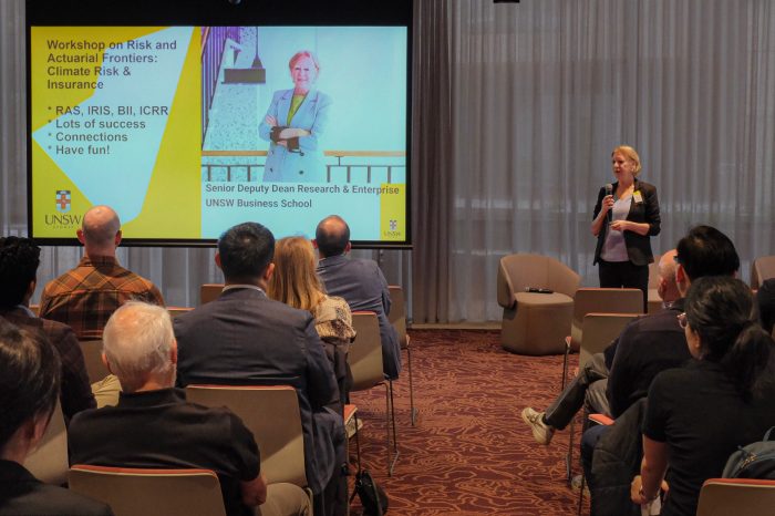 A speaker holding a microphone stands in front of seated workshop attendees