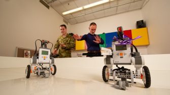 Officer Cadet Todd Baldwin (left) and Spike (Dr. Michael Barlow - right) playfully brainstorm alternate, gesture-based control schemes for the robots picture in the foreground; within the Machine Learning & Developmental Robotics (MLDR) lab.School of Engineering and Information Technology (SIET) Machine Learning & Developmental Robotics (MLDR).