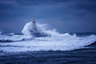 Big wave against old Lighthouse in the port of Ahtopol, Black Sea, Bulgaria on a moody stormy day. Danger, dramatic scene.