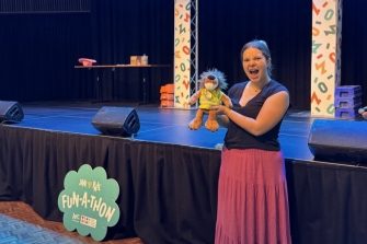 Student posing with a plushie in front of the Fun-a-Thon stage at the Roundhouse