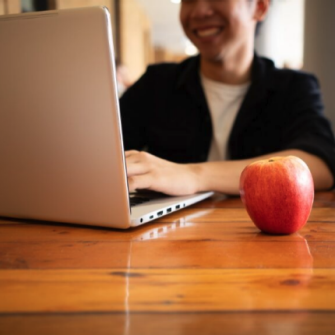 A person using a laptop with an apple beside them