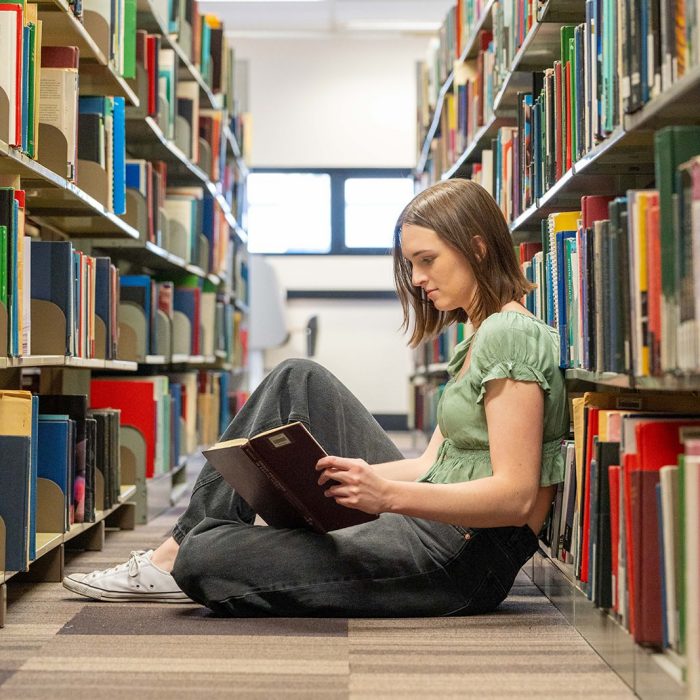 A student looking at a book in an aisle of the library